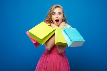 Bright emotional portrait of a beautiful young woman posing with shopping bags, isolated on blue background
