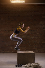 Young fit caucasian woman doing a box jump exercise. Muscular woman doing a box squat at the gym.