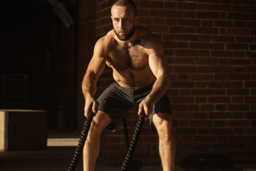 Fototapeta na wymiar Sport concept. Caucasian athlet with naked torso with rope in functional training at outdoor gym in a crossfit workout over brick wall background.