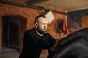 Face of a handsome european bearded man turning over heavy tire in gym. Sport concept