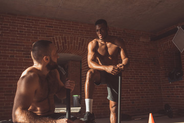 Two interracial sportsmen resting between repetitions in crossfit workout, African shirtless guy...