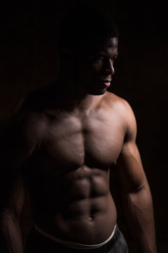 Handsome African American bodybuilder man, with naked muscular torso posing against red brick wall. Low key photo.