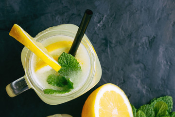 Refreshing lemonade drink with lemon slice and mint in the jar on dark background, top view
