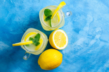 Refreshing lemonade drink with lemon slice and mint in the jar on a blue background, top view