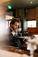Confident thoughtful artist, wealthy man having a cup of tea, enjoying minutes of rest while waiting someone in the modern popular restaurant