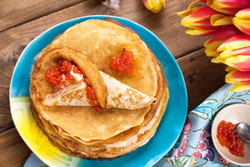 pancakes with caviar and butter, a bouquet of fresh tulips and a wooden background. Traditional Russian food for carnival. Top view.