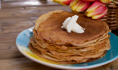 Russian pancakes with butter on a wooden background. A bouquet of fresh spring tulips and traditional Russian food. Free space for text.