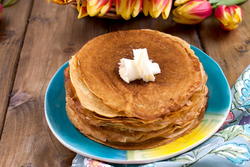 Russian pancakes with butter on a wooden background. A bouquet of fresh spring tulips and traditional Russian food. Free space for text.