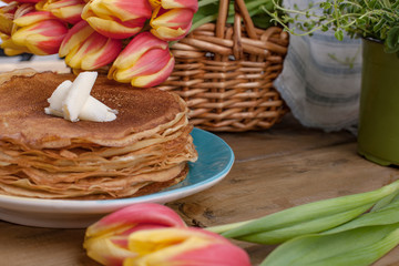 Russian pancakes with butter on a wooden background. A bouquet of fresh spring tulips and traditional Russian food. Free space for text.