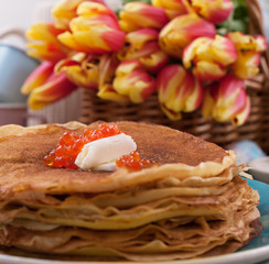 Russian pancakes with butter on a wooden background. A bouquet of fresh spring tulips and traditional Russian food. Free space for text.