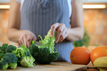 Close up of woman cutting broccoli with kitchen knife on cutting board