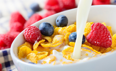 Pouring milk into bowl of Corn Flakes with berries