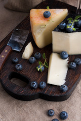 White pecorino cheese and blueberries. Traditional Italian hard cheese and a glass of red wine. Wooden background and dark style photo. Cheese typical of sardinia. Copy space.