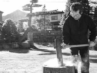 An older man making mochi in the winter with steaming hot rice.