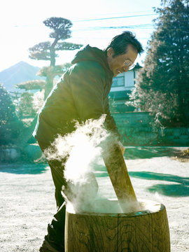 An Older Man Making Mochi In The Winter With Steaming Hot Rice.