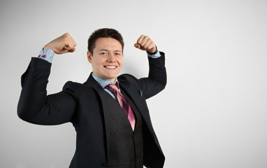 Young attractive guy businessman in suit on gray background with muscular arms, champion and superhero. Success in business.