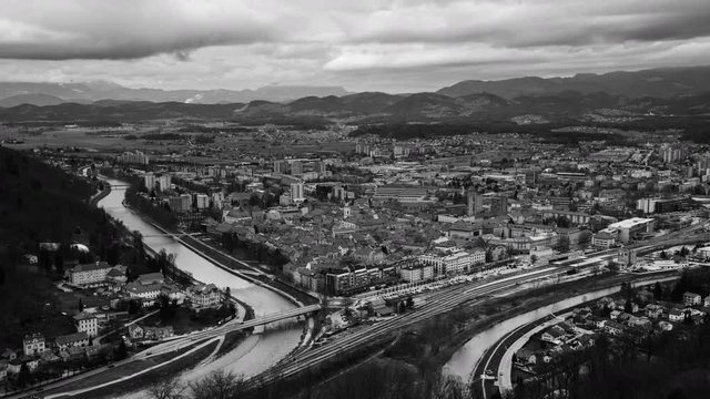 Celje, Slovenia. Car traffic in Celje, Slovenia. Bridge over the Savinja river. Aerial view of city historical center from the castle. Time-lapse during the cloudy day with mountains. Black and white