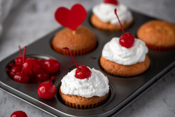 Homemade muffins with cream and cherry on the muffin tin.