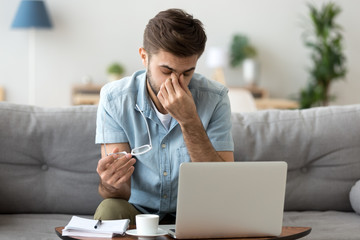 Tired young man feeling eye strain headache after computer work