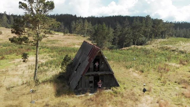 Aerial: Young Woman and Men at Ruinous Hut on Meadow