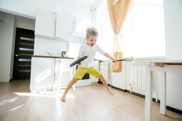 Fototapeta na wymiar funny European little boy chef dancing,Happy weekend, boy wants to make pancakes, but the frying pan are too gay, he decided to have fun holding wooden spoons in his hands, having fun while cooking