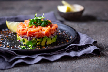 Raw salmon, avocado purple onion salad served in culinary ring on black plate. Black concrete background