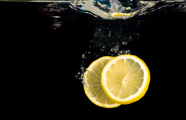 Slices of lemon thrown into water on a black background
