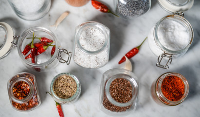 Various spices in glass jars on a white marble table flat lay