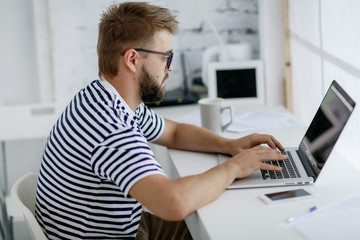 Young business man,  sitting at desk at home and looking at open laptop display.