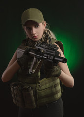the girl in military special clothes posing with a gun in his hands on a dark background in the haze