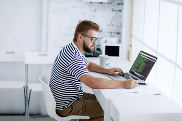 Young business man,  sitting at desk at home and looking at open laptop display.