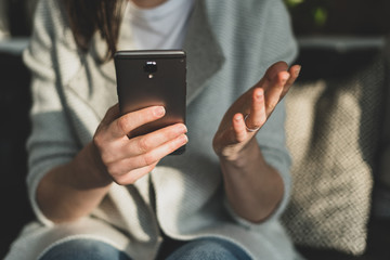 Confused woman holding cellular in hands and gesturing open palm
