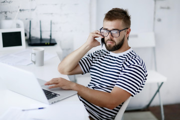 Freelancer man at work in office and looking at open laptop workstation.