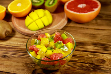 Tasty fruit salad in glass bowl and fresh fruits on the wooden table