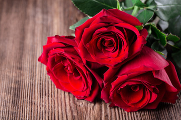 Three red roses on wooden background with copyspace.