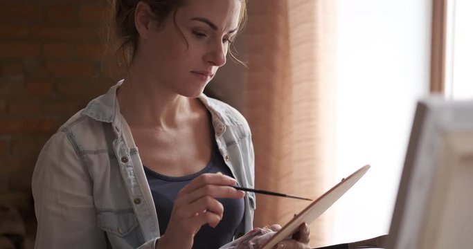 Skilled female artist holding palette and painting on canvas