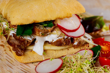 Sandwich with meat, radish, onions, cheese, sauce and lettuce on a wooden board on cherry tomatoes.