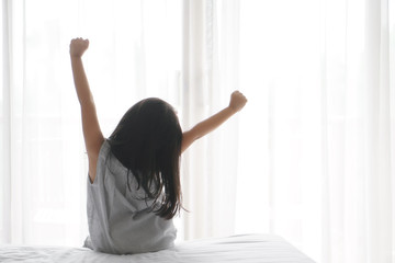 Fototapeta na wymiar Asian child cute relax or kid girl wake up or woke up with stretch oneself after sleep for refreshing in morning on white bed and window with curtain in bedroom at home or hotel and resort on holiday