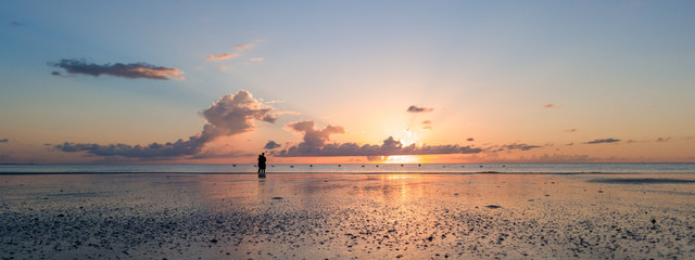 Couple embracing on beach watching sunrise as flock of pelicans fly by