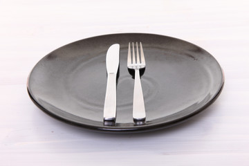白い木製テーブルに置かれた黒い皿とカトラリーによる食事終了の合図