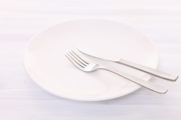 白い木製テーブルに置かれた白い皿とカトラリーによる食事終了の合図