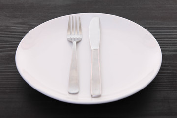 黒い木製テーブルに置かれた白い皿とカトラリーによる食事終了の合図