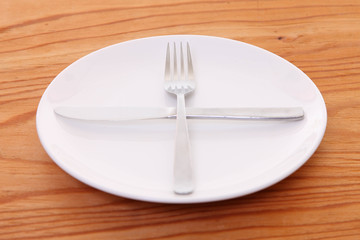 木製テーブルに置かれた白い皿とカトラリーによる次の料理を待機の合図
