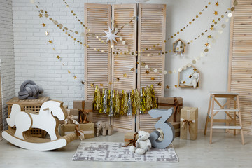 Birthday gold and silver decorations with gifts, toys, garlands and figure for little baby party on a white bricks background.