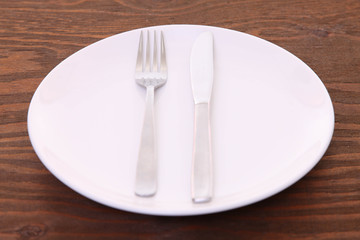 茶色い木製テーブルに置かれた白い皿とカトラリーによる食事終了の合図