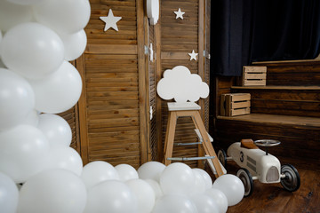 Fototapeta na wymiar Birthday white decorations with balloons, stars, clouds and toy retro car for little baby on a dark brown background.