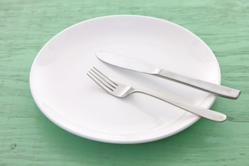 緑の木製テーブルに置かれた白い皿とカトラリーによる食事終了の合図