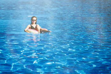 Young pretty girl sails on a floating ring in the pool with clean, blue water in the resort hotel. The concept of recreation and healthy lifestyle.