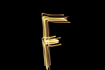 Long exposure, light painting photography.  Letter f in a vibrant neon metallic yellow gold colour against a black background.  Alphabet series.