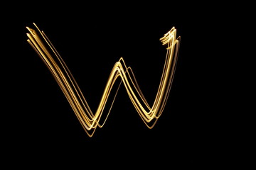Long exposure, light painting photography.  Letter w in a vibrant neon metallic yellow gold colour against a black background.  Alphabet series.